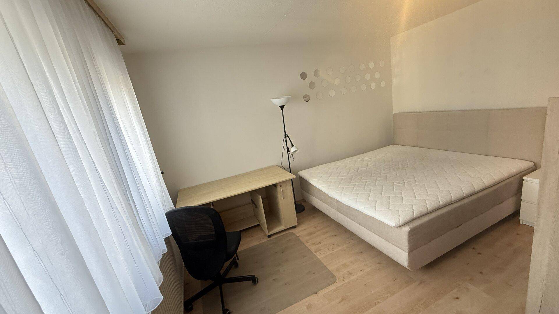 Schlafbereich in einem Studio-Apartment mit Doppelbett, Schreibtisch und großem Fenster.