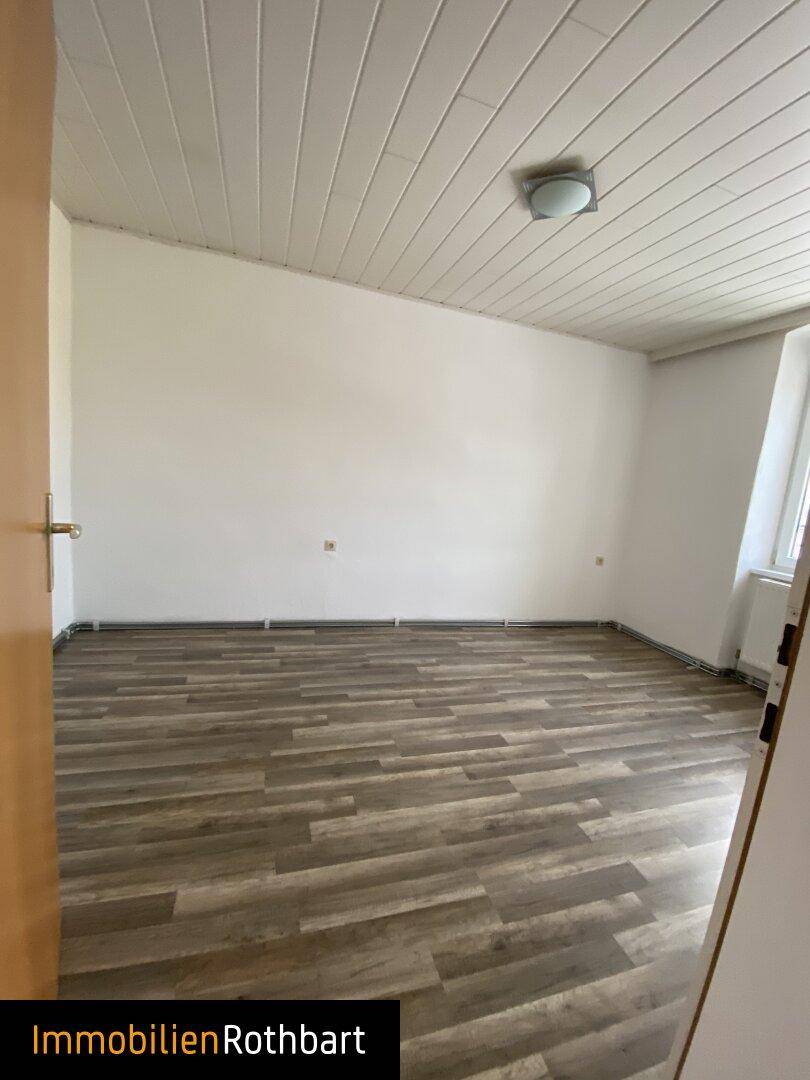 Geräumiges Zimmer mit Laminatboden und weißen Wänden, das auf neue Bewohner wartet.