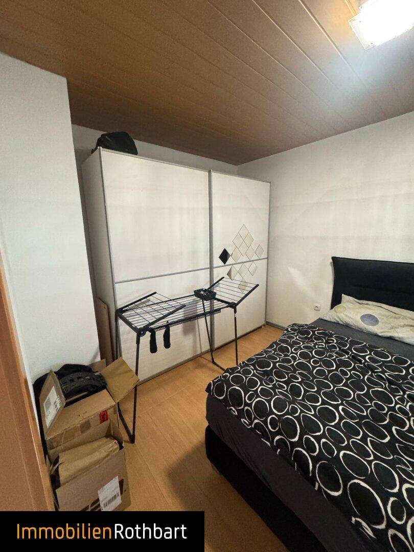 Schlafzimmer mit Bett, weißem Kleiderschrank und Laminatboden, bereit für persönliche Gestaltung.