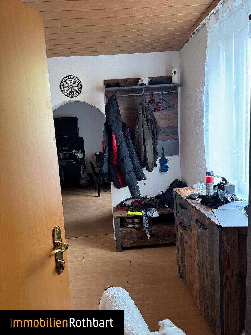 Eingangsbereich mit Garderobe und Holzmöbeln, der zu einem weiteren Raum führt.