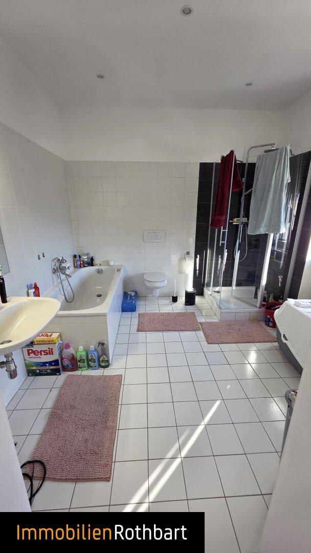 Helles Badezimmer mit weißen Fliesen, Badewanne, Dusche und Toilette, gut beleuchtet.
