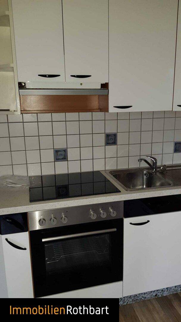 Detailansicht der weißen Einbauküche mit Kochfeld, Backofen und Spüle, umgeben von Fliesen.