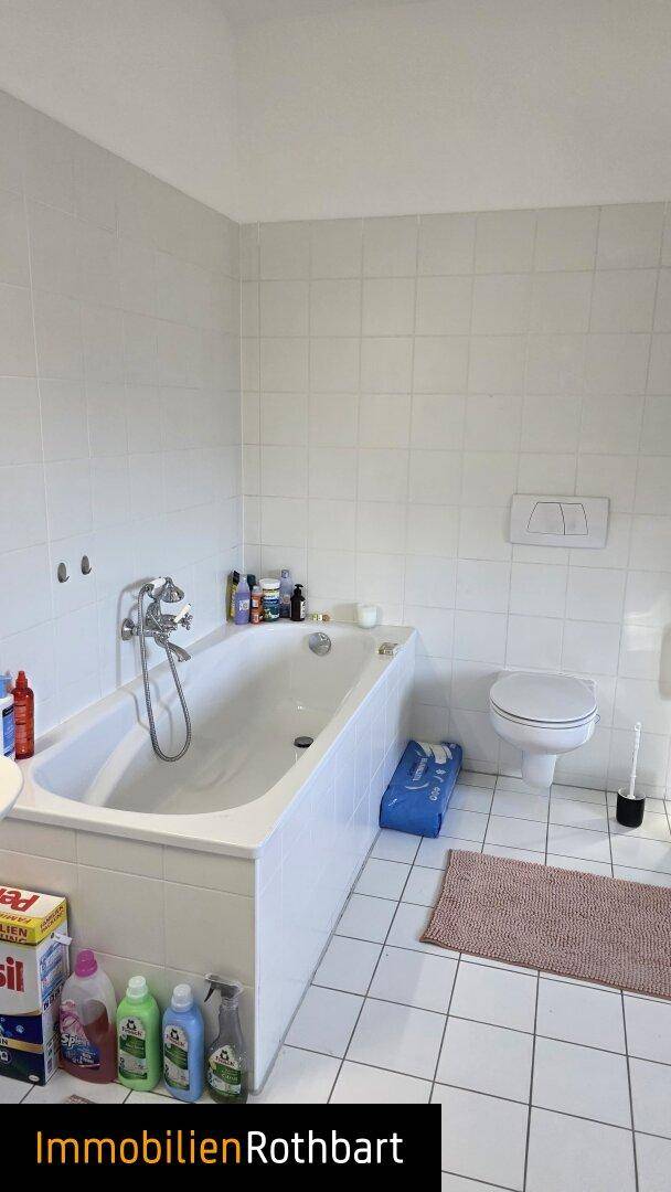 Helles Badezimmer mit Badewanne, wandhängendem WC und weißen Fliesen an Wänden und Boden.