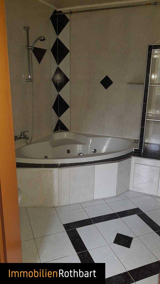 Badezimmer mit Eckbadewanne und integrierter Dusche, gefliest in Schwarz-Weiß-Muster.