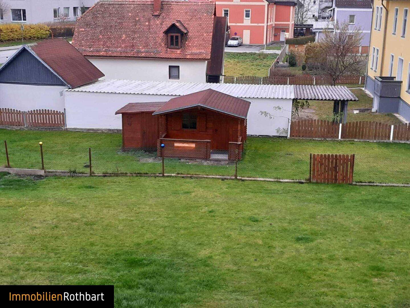 Großer Rasengarten mit einem kleinen Holzschuppen und einem Zaun, umgeben von anderen Häusern.