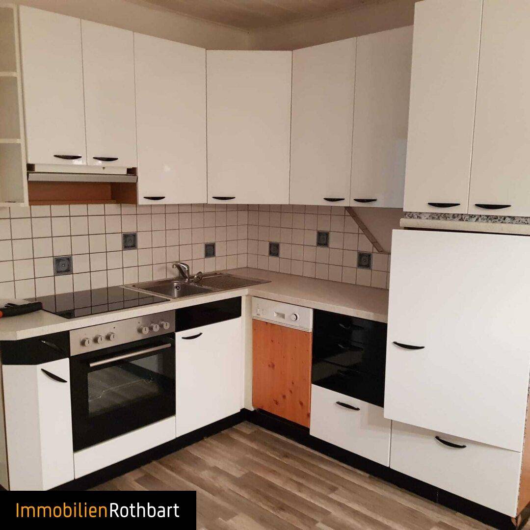 Weiße Einbauküche mit Kochfeld, Backofen und Spülmaschine, gefliestem Spritzschutz und Laminatboden.