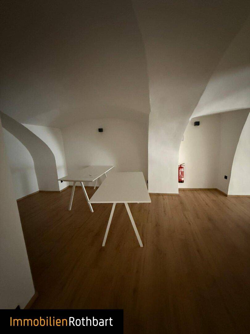 Großer, heller Bürobereich mit gewölbter Decke, Holzboden und mehreren Arbeitstischen.