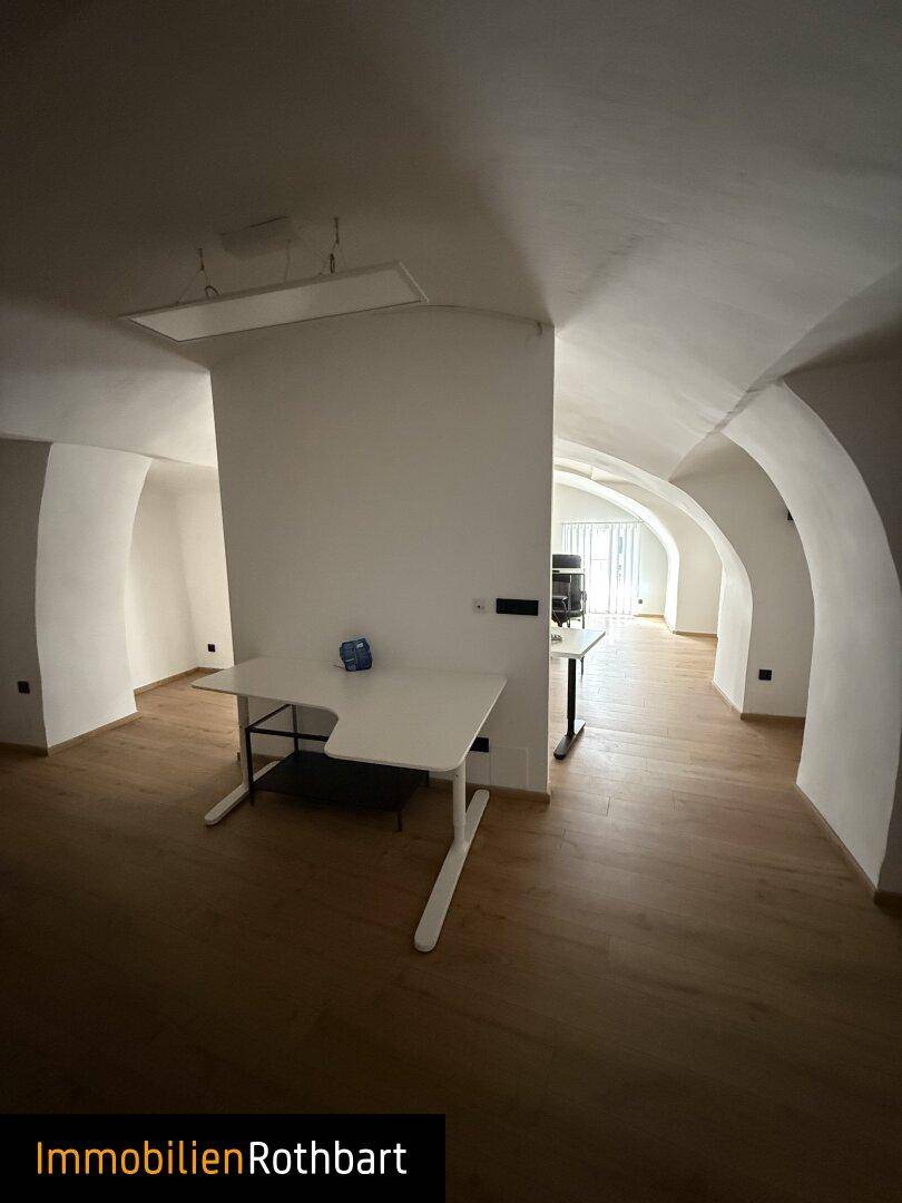 Langer Bürogang mit gewölbten Decken, Holzboden und mehreren Arbeitsbereichen.