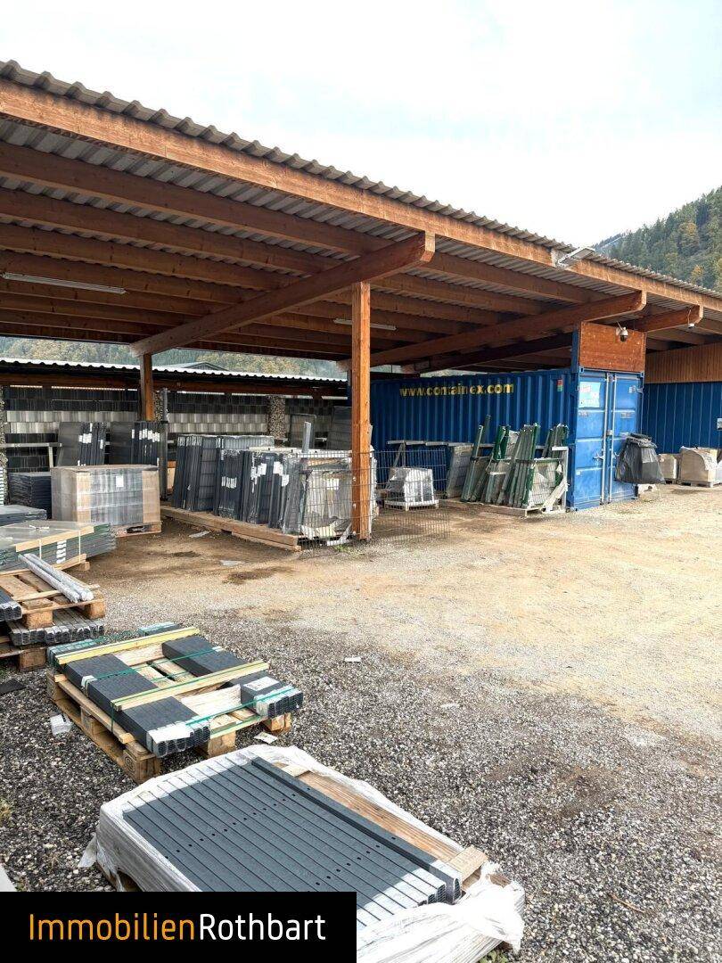 Überdachter Außenbereich mit Holzkonstruktion und gelagerten Waren vor bergiger Kulisse.