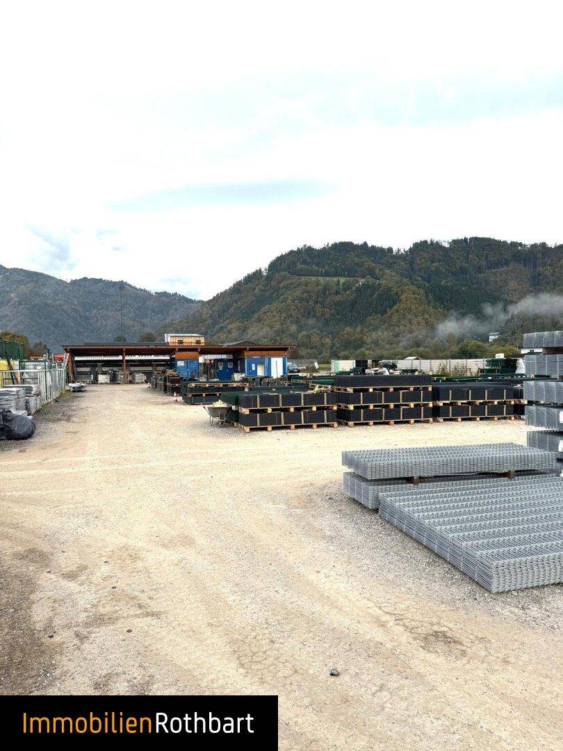 Weitläufiger Lagerplatz im Freien mit verschiedenen Materialien und Blick auf die bewaldeten Berge.