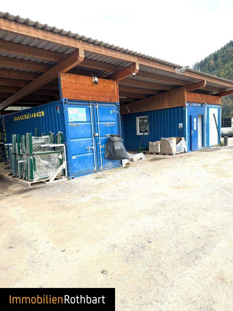Überdachter Bereich mit blauen Schiffscontainern, die als Lagerräume dienen, und Holzbalken.