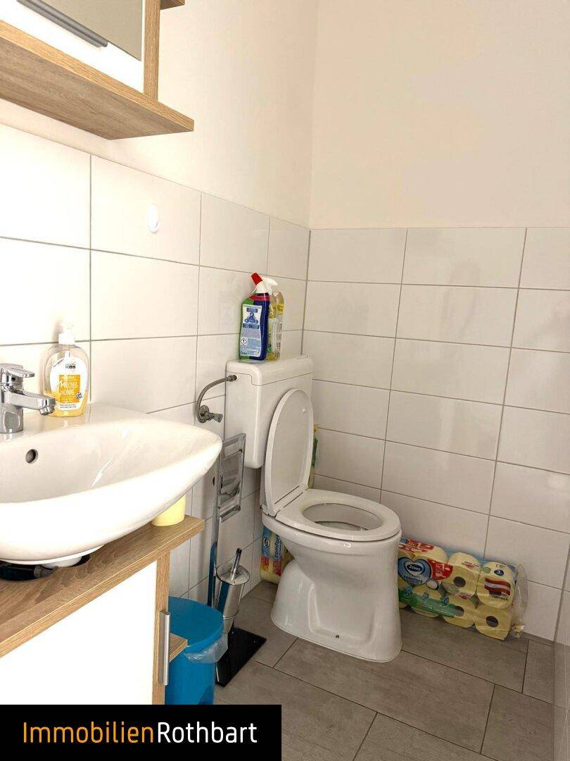 Kleiner Toilettenraum mit Waschbecken, WC und weißen Wandfliesen.