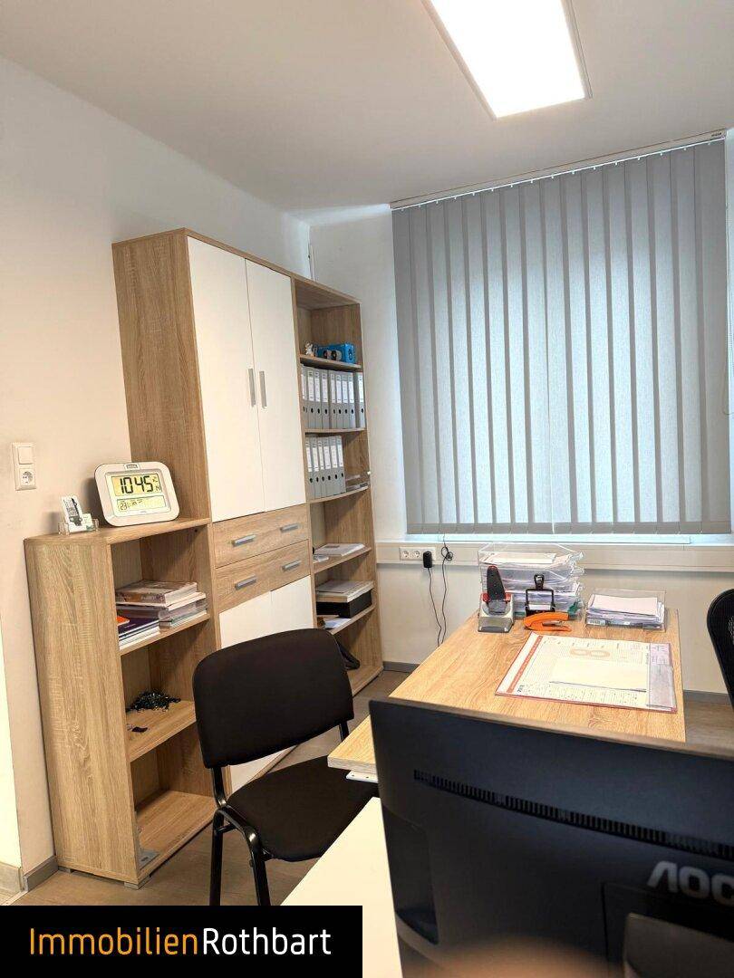Büro mit großem Holzschrank, Regalen und einem Arbeitsplatz, gut beleuchtet.