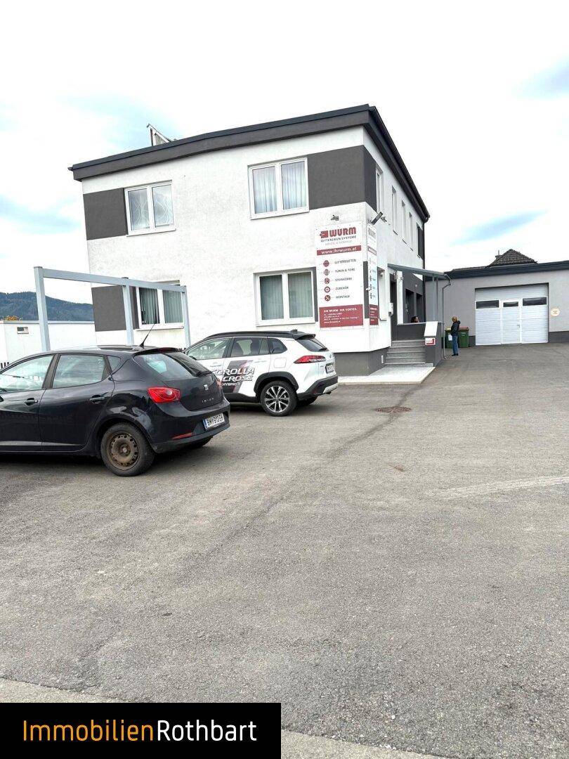 Gewerbegebäude mit Parkplätzen davor und einer Garageneinfahrt auf der rechten Seite.