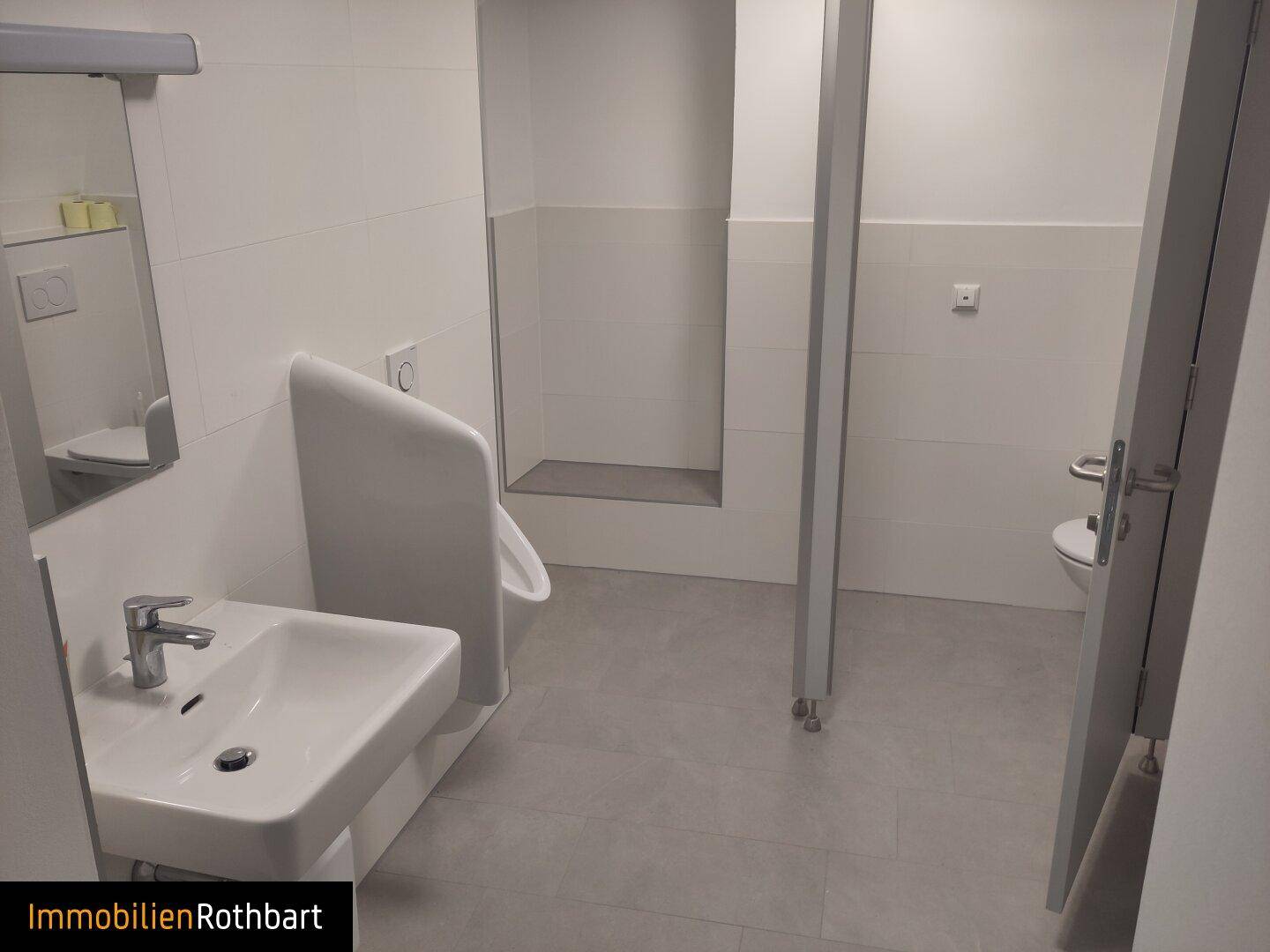 Modernes Badezimmer mit Urinal, Waschbecken und gefliesten Wänden in neutralen Farben.