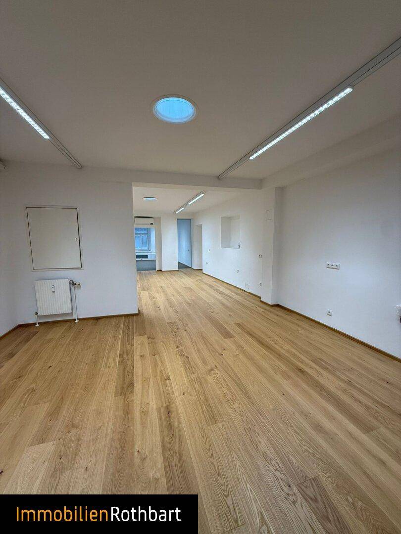 Heller, leerer Büroraum mit modernem Holzfußboden und Deckenbeleuchtung.