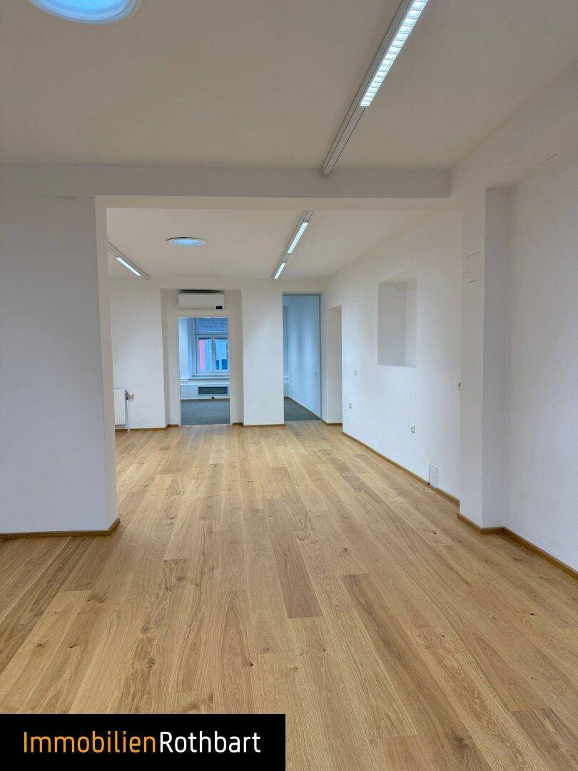 Geräumiger Bürobereich mit hellem Holzparkett und integrierter Deckenbeleuchtung.