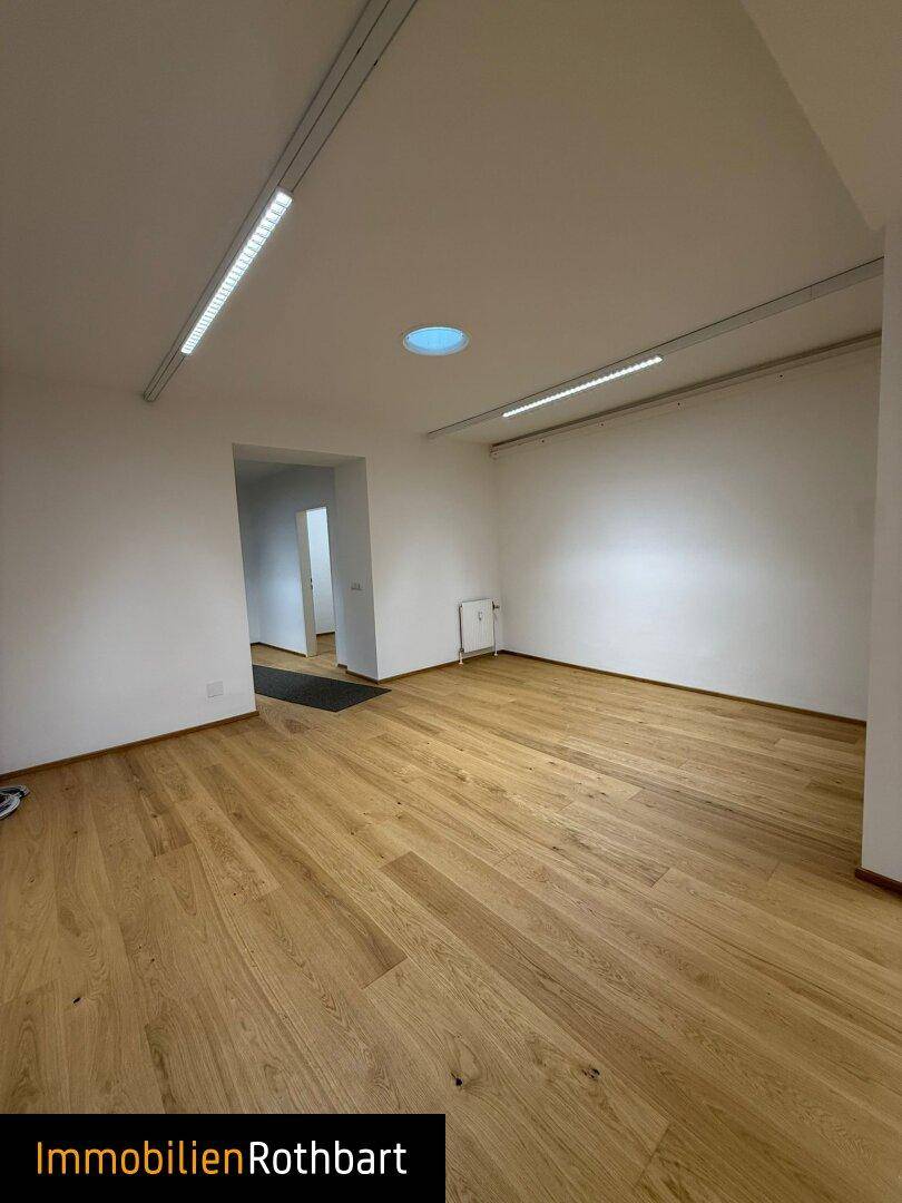 Heller und geräumiger Büroraum mit Holzboden und Deckenbeleuchtung, bereit zur Gestaltung.