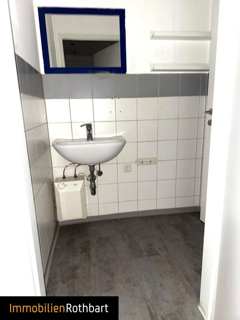 Gästetoilette mit Waschbecken und Spiegel, gefliesten Wänden in Weiß und Grau, sowie dunklem Boden.