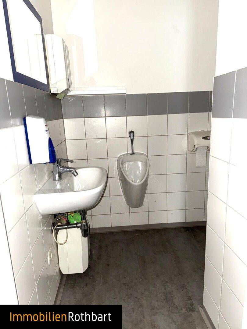 Funktionale Gästetoilette mit Urinal, Waschbecken und gefliesten Wänden in Weiß und Grau.