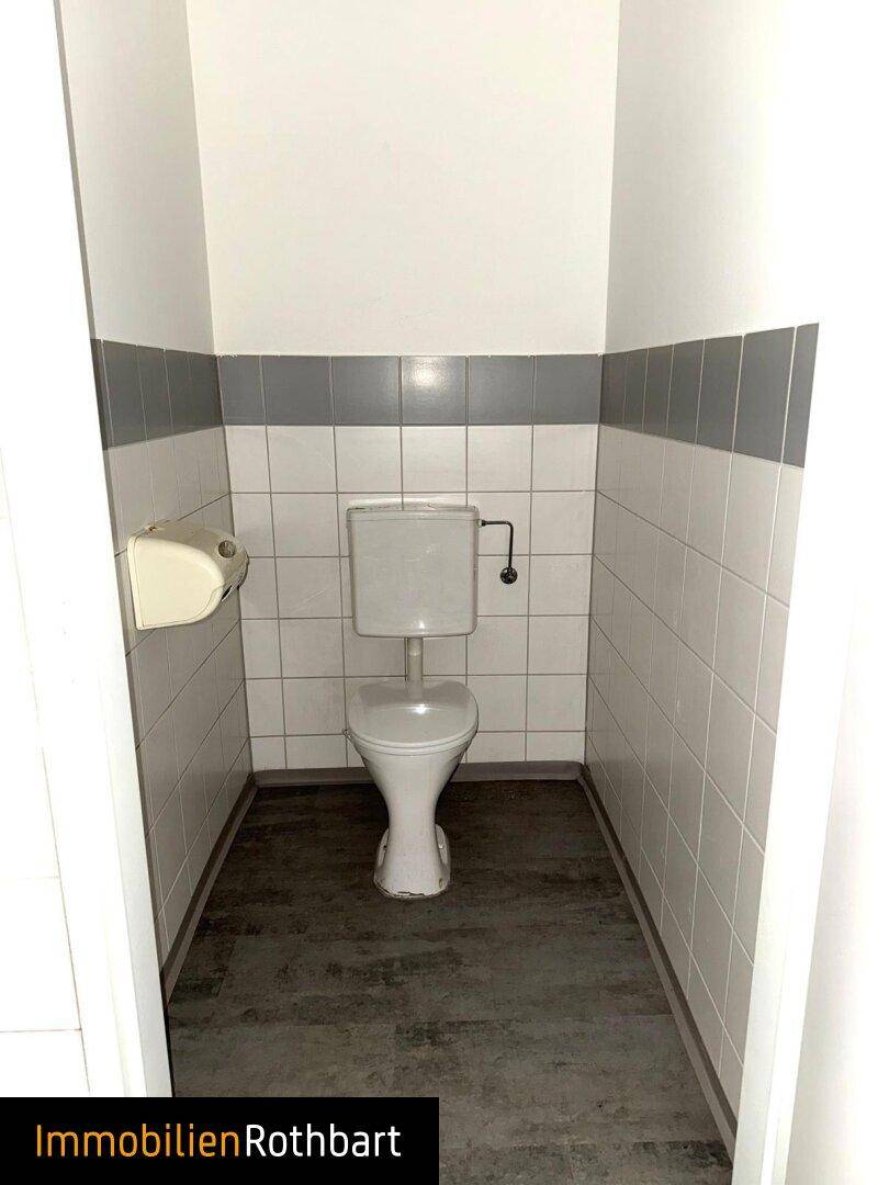 Schlichte Gästetoilette mit WC und gefliesten Wänden in Weiß und Grau, mit dunklem Boden.