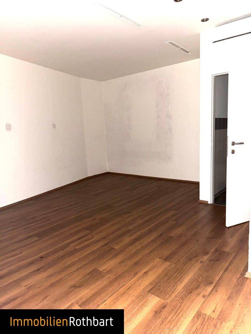 Heller Geschäftsraum mit Laminatboden und Zugang zu einem Nebenraum, ideal für Büro oder Lager.