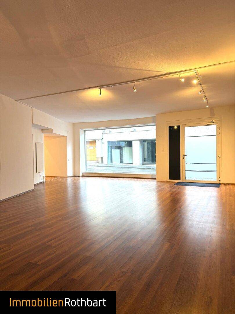 Großer Gewerberaum mit Schaufensterfront und Eingangstür, bietet viel Tageslicht und Sichtbarkeit zur Straße.
