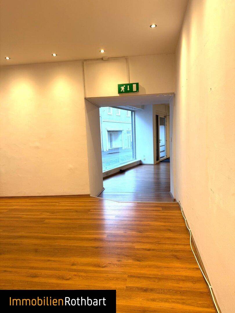 Blick aus dem Gewerberaum durch einen Durchgang zur Straße, mit deutlichem Ausgangsschild über dem Eingang.