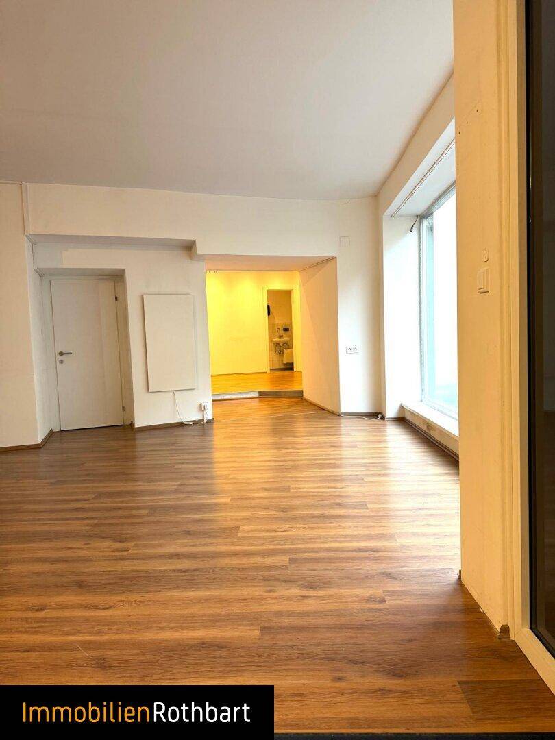 Geräumiger Gewerberaum mit Zugang zu einem weiteren Bereich und einem Fenster, das Tageslicht hereinlässt.