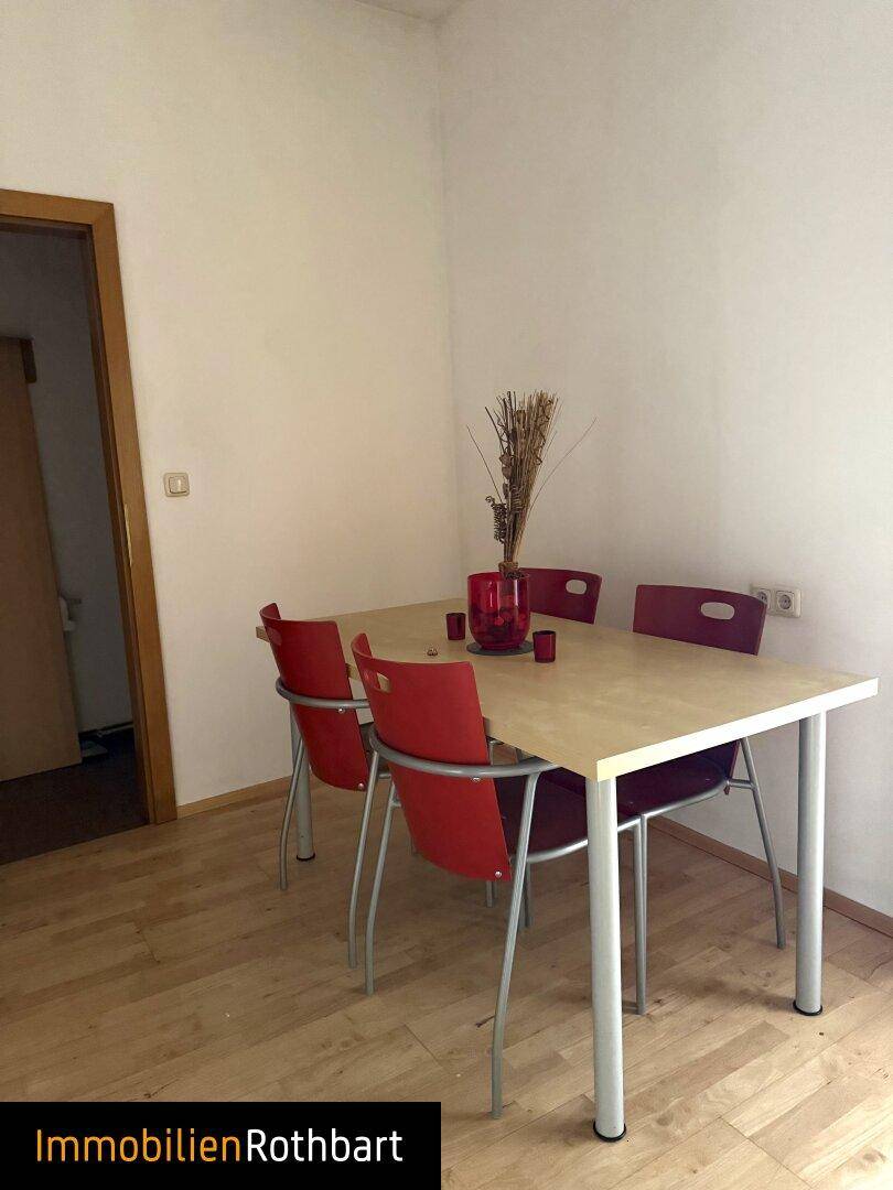 Kleiner Essbereich mit modernem Holztisch, roten Stühlen und Holzboden.