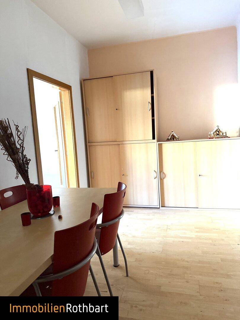 Essbereich mit hellen Holzschränken, modernem Tisch und roten Stühlen.
