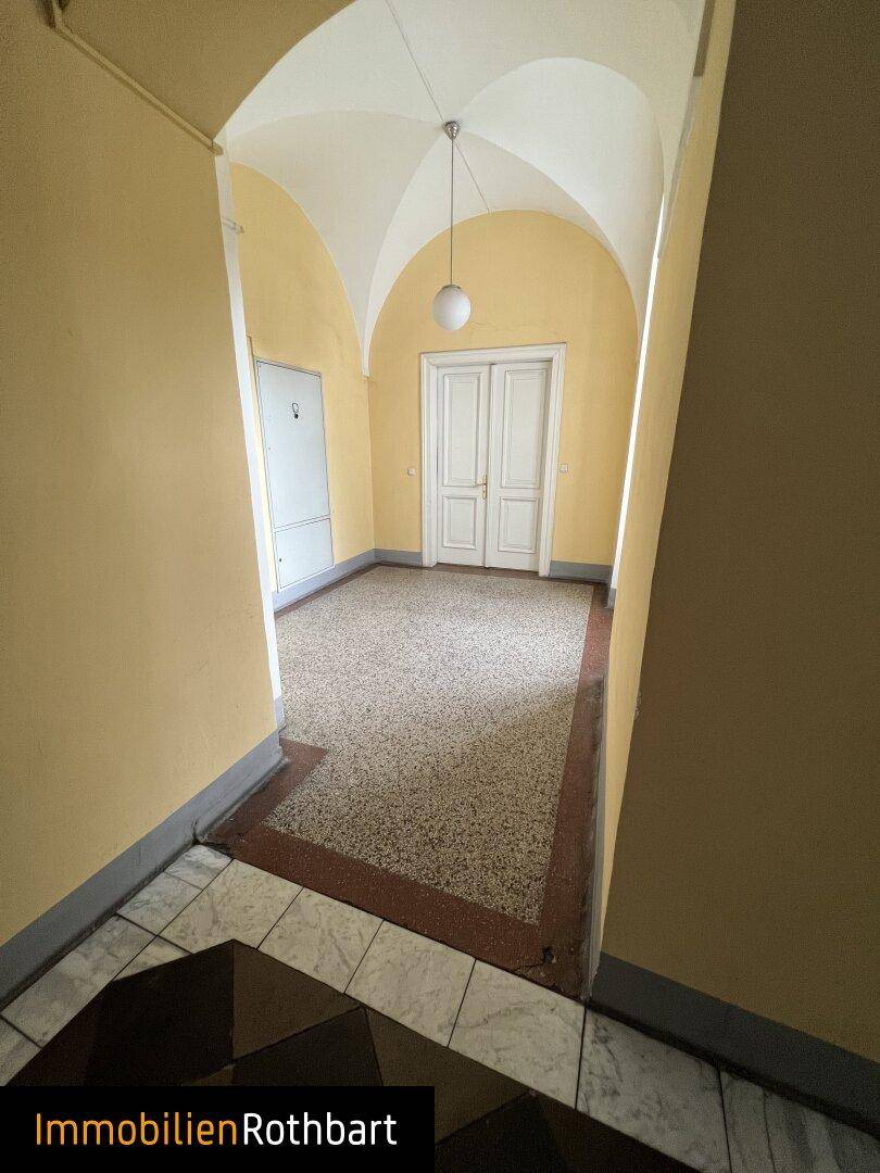 Historischer Flur mit gelben Wänden, einem Gewölbedecke und einem gemusterten Terrazzoboden, führt zu Doppeltüren.