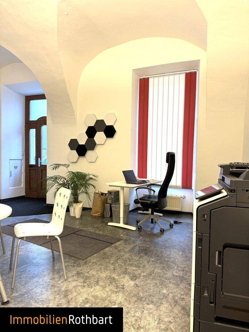 Büro mit gewölbter Decke, großem Fenster mit Jalousien und modernen Akustikpaneelen an der Wand.