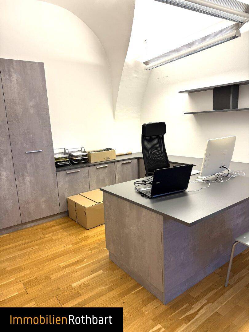 Büro mit Holzboden, gewölbter Decke und modernen grauen Schränken sowie einem passenden Schreibtisch.