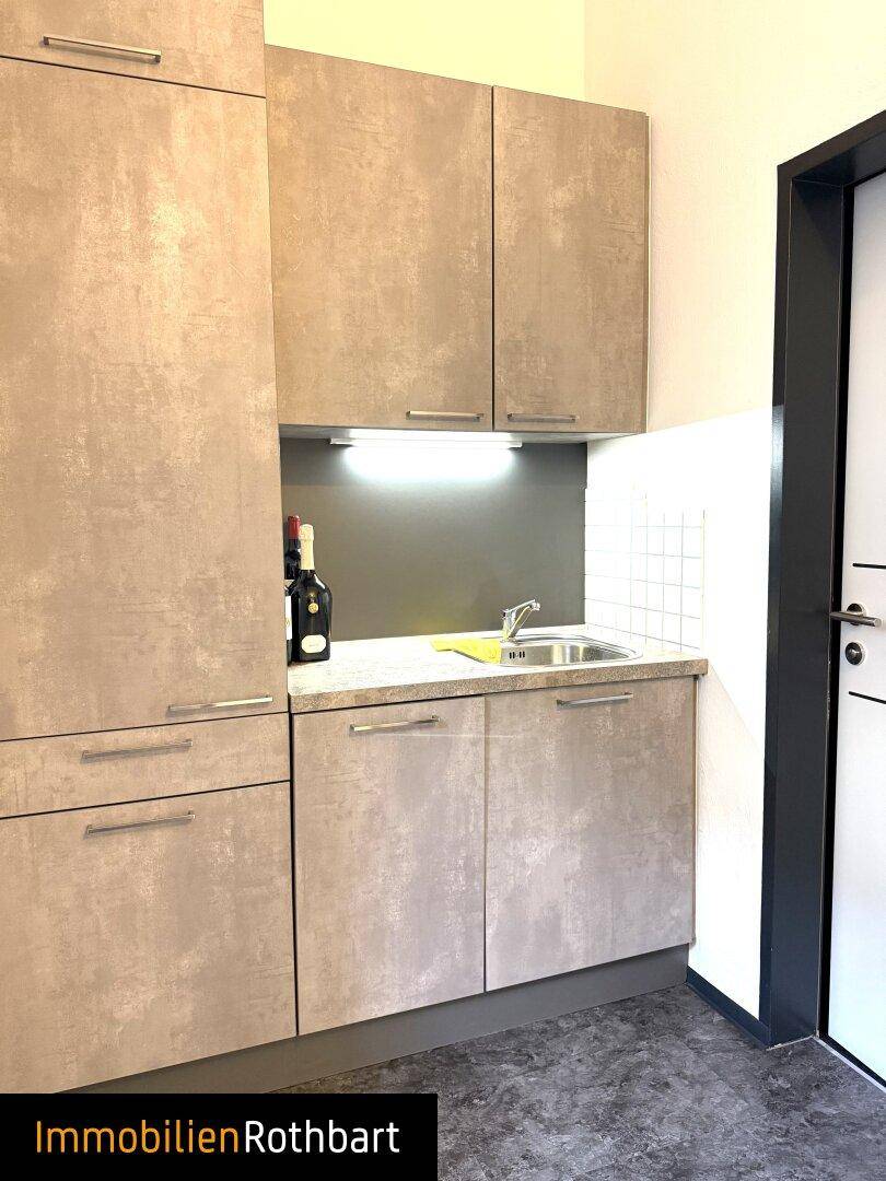 Kleine Küchenzeile mit grauen Schränken, Spüle und einer gefliesten Rückwand über der Arbeitsplatte.