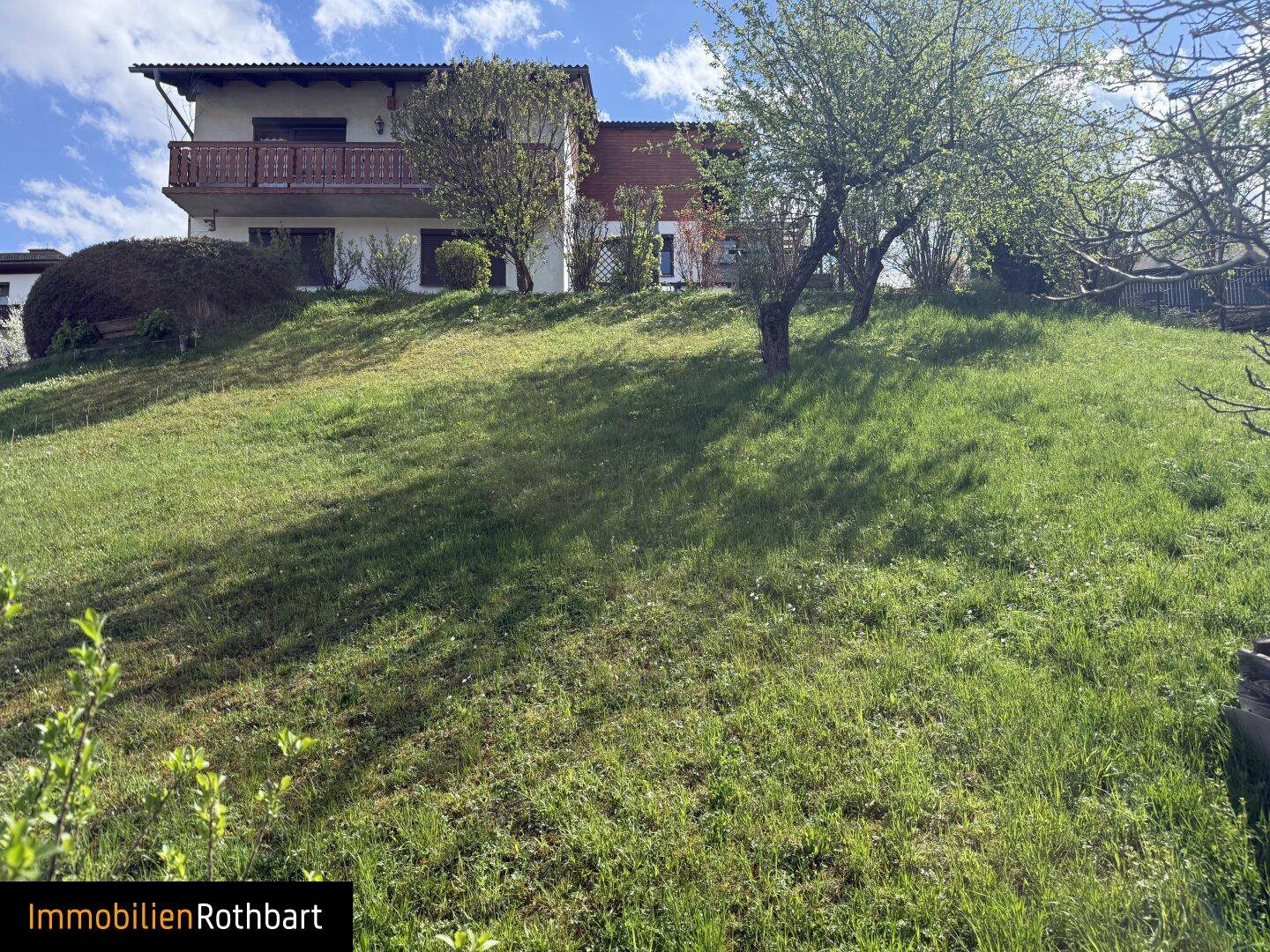 Haus in Hanglage mit großem Rasenbereich und Bäumen im Vordergrund.