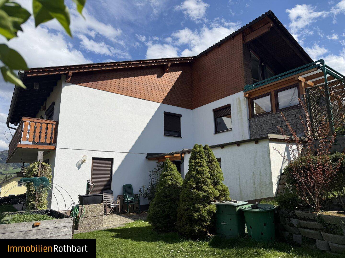 Rückansicht des Hauses mit Balkon, Holzverkleidung und kleinem Gemüsegarten.