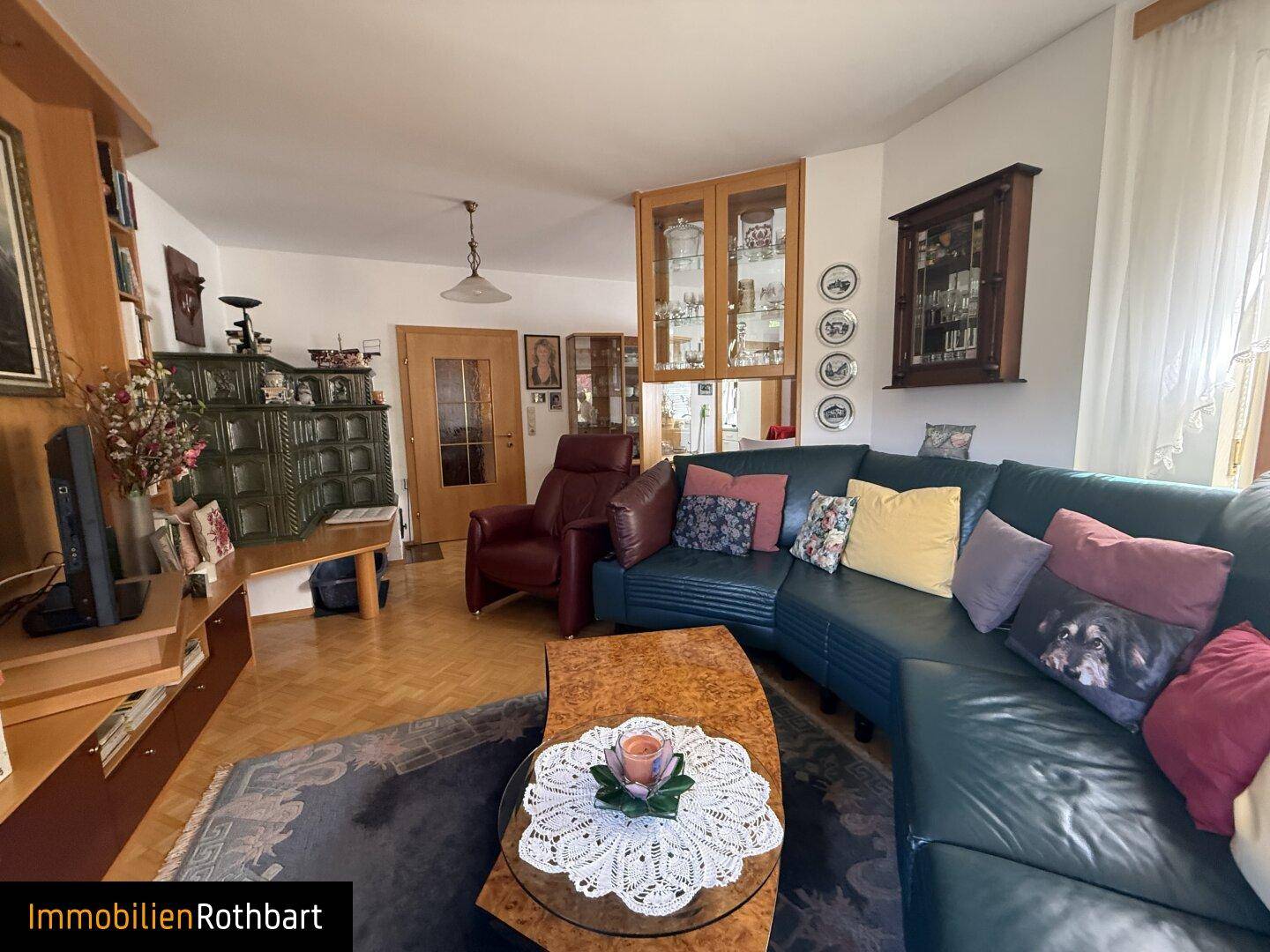 Wohnzimmer mit bequemer Ledercouch, Holzboden und traditionellem Kachelofen.