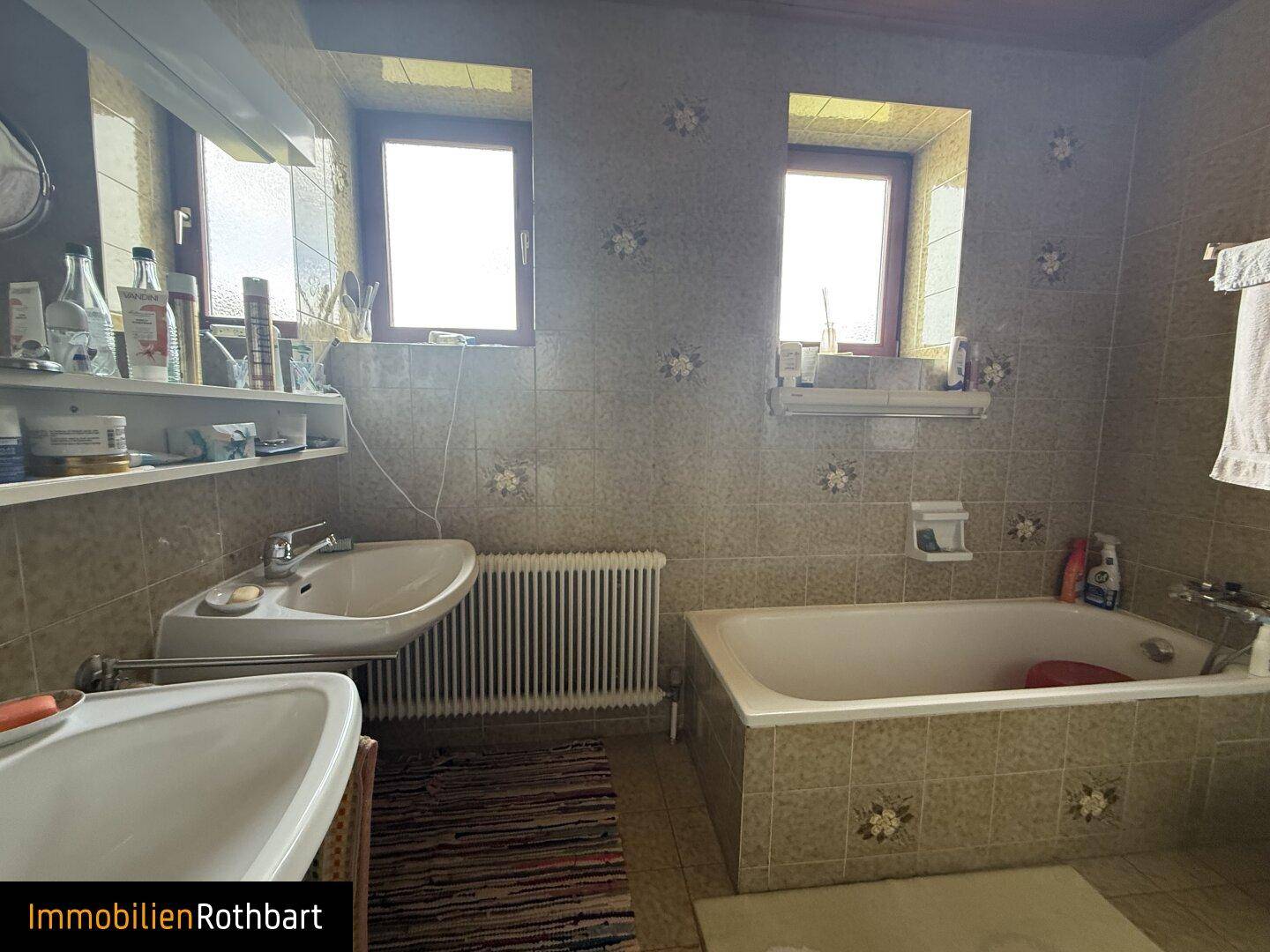 Badezimmer mit zwei Fenstern, Badewanne und Waschbecken im traditionellen Stil.