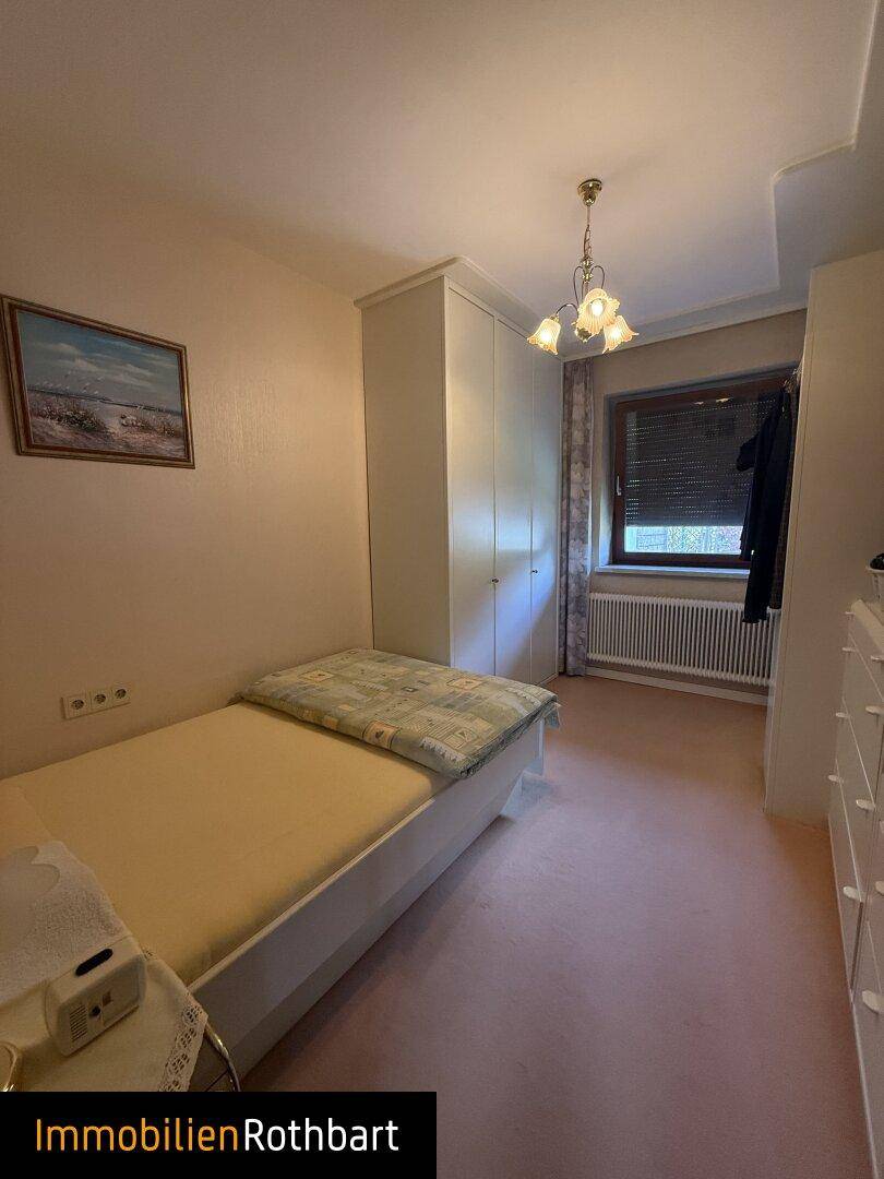 Helles Schlafzimmer mit Einzelbett, Kleiderschrank und Teppichboden.