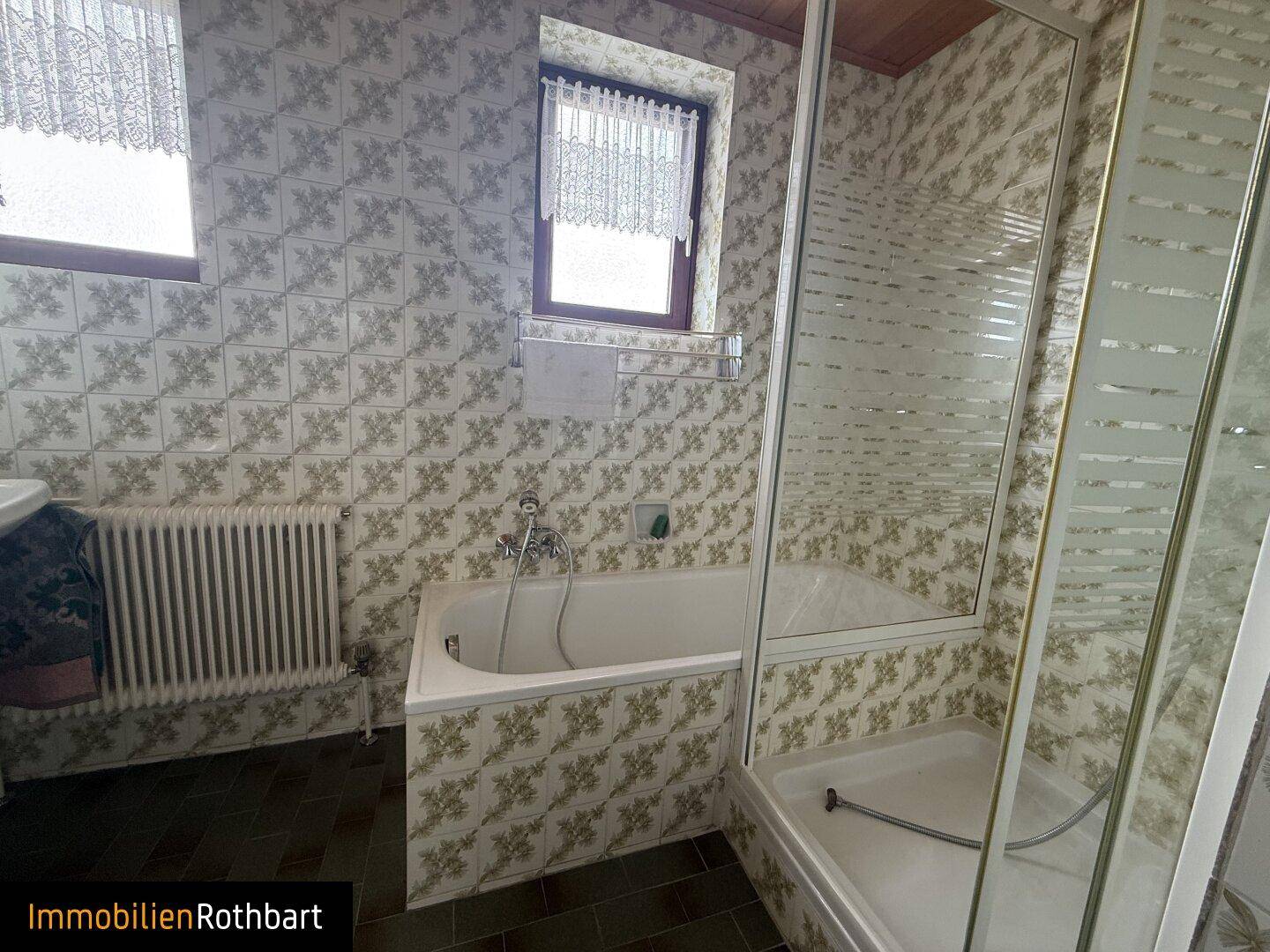 Badezimmer mit Badewanne, Duschkabine und gemusterten Fliesen im 80er-Jahre-Stil.
