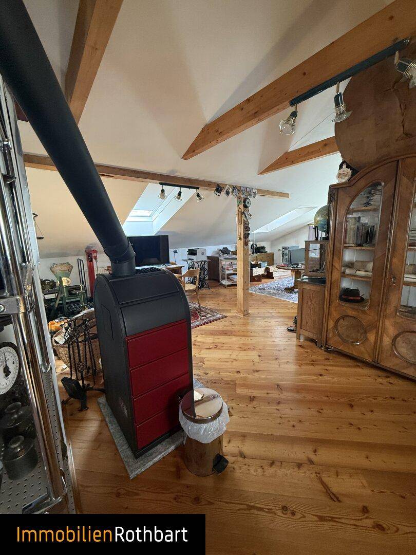 Ausgebauter Dachboden mit Holzboden, freiliegenden Balken und Kaminofen.