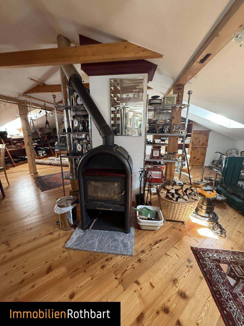 Offener Dachbodenbereich mit Kaminofen, Holzregalen und Holzboden.
