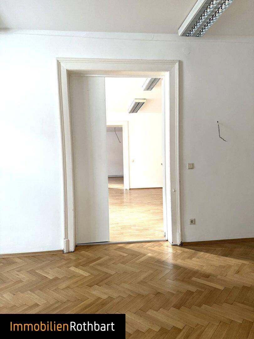 Offener Durchgang zu einem weiteren hellen Raum mit Holzparkett und weißen Wänden.