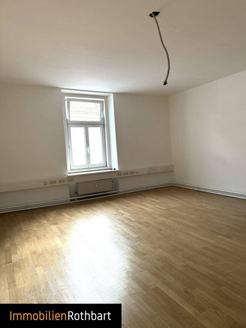 Heller, leerer Raum mit Holzparkett, weißen Wänden und einem Fenster, bereit zur Gestaltung.