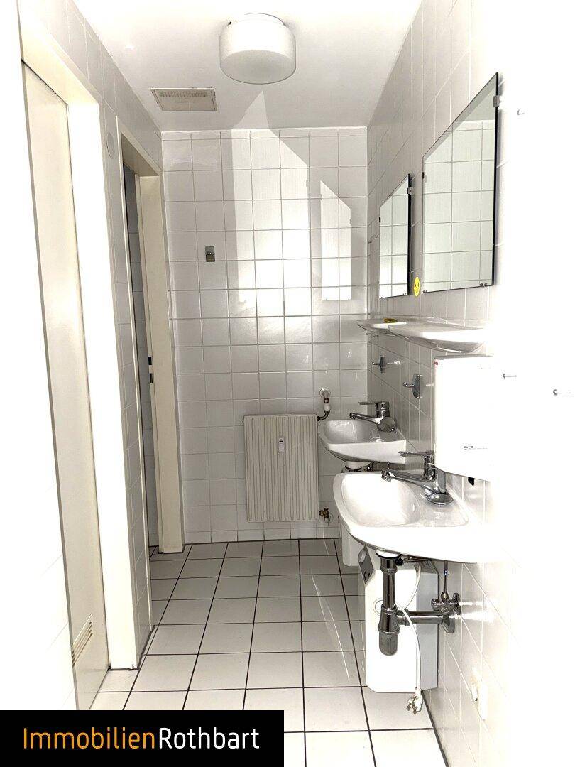 Helles Badezimmer mit weißen Fliesen, zwei Waschbecken, Spiegeln und Heizkörper.