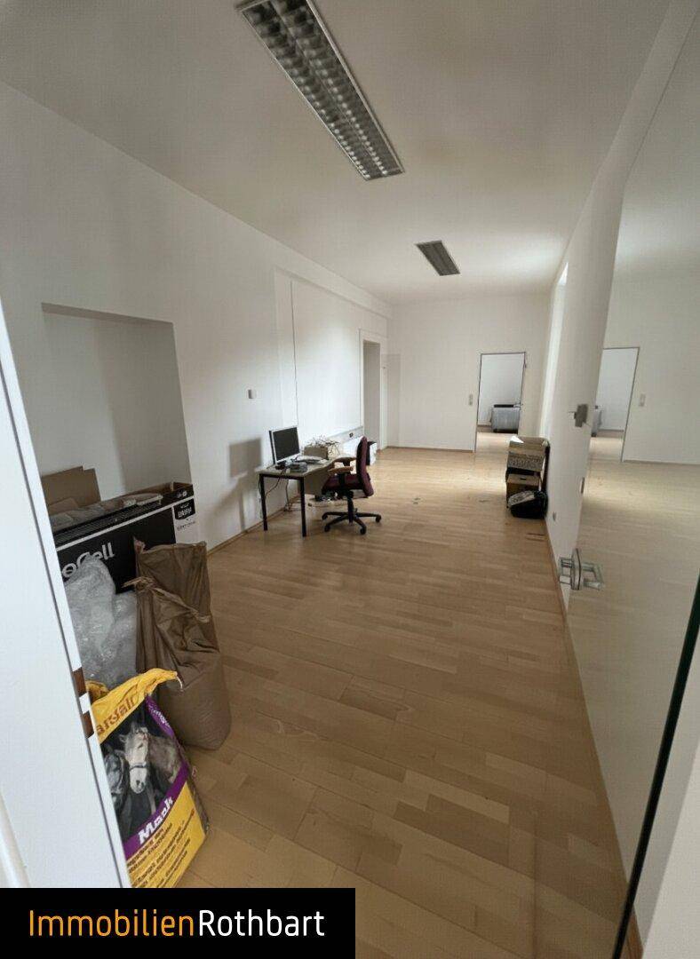 Langer, heller Büroraum mit Holzfußboden, weißen Wänden und einigen Büromöbeln, ideal für Arbeitsbereiche.