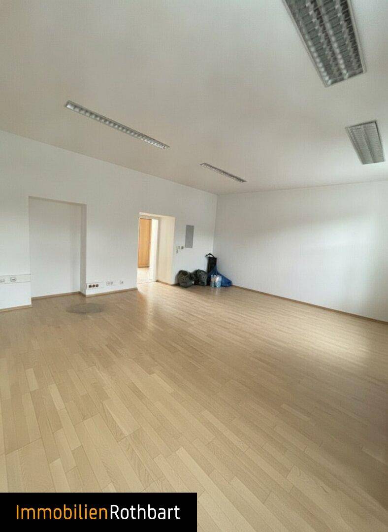 Großer, leerer Raum mit hellem Holzfußboden und weißen Wänden, ideal für flexible Büronutzung oder Besprechungen.