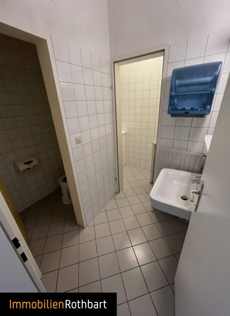 Kleiner Toilettenbereich mit weißen Fliesen an Wänden und Boden, ausgestattet mit Waschbecken und Papierspender.
