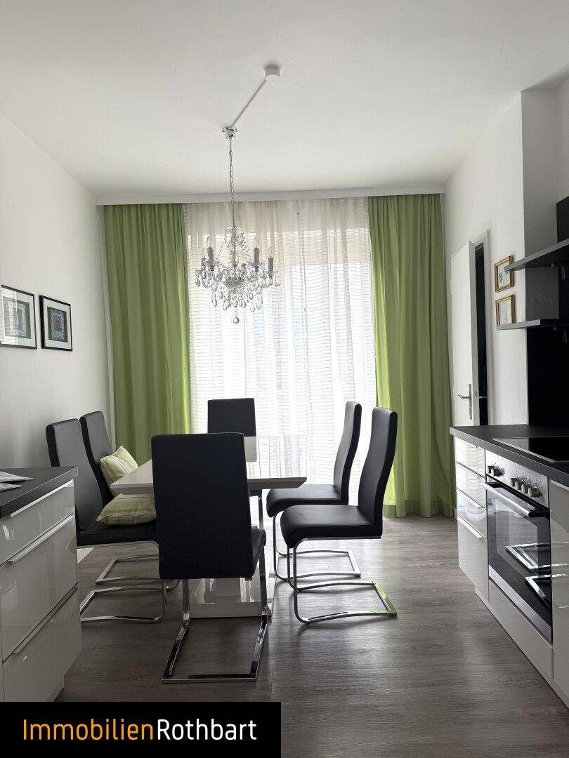 Heller Küchen- und Essbereich mit modernem Design, Laminatboden und Kronleuchter. Grüne Vorhänge rahmen die Fenster ein.